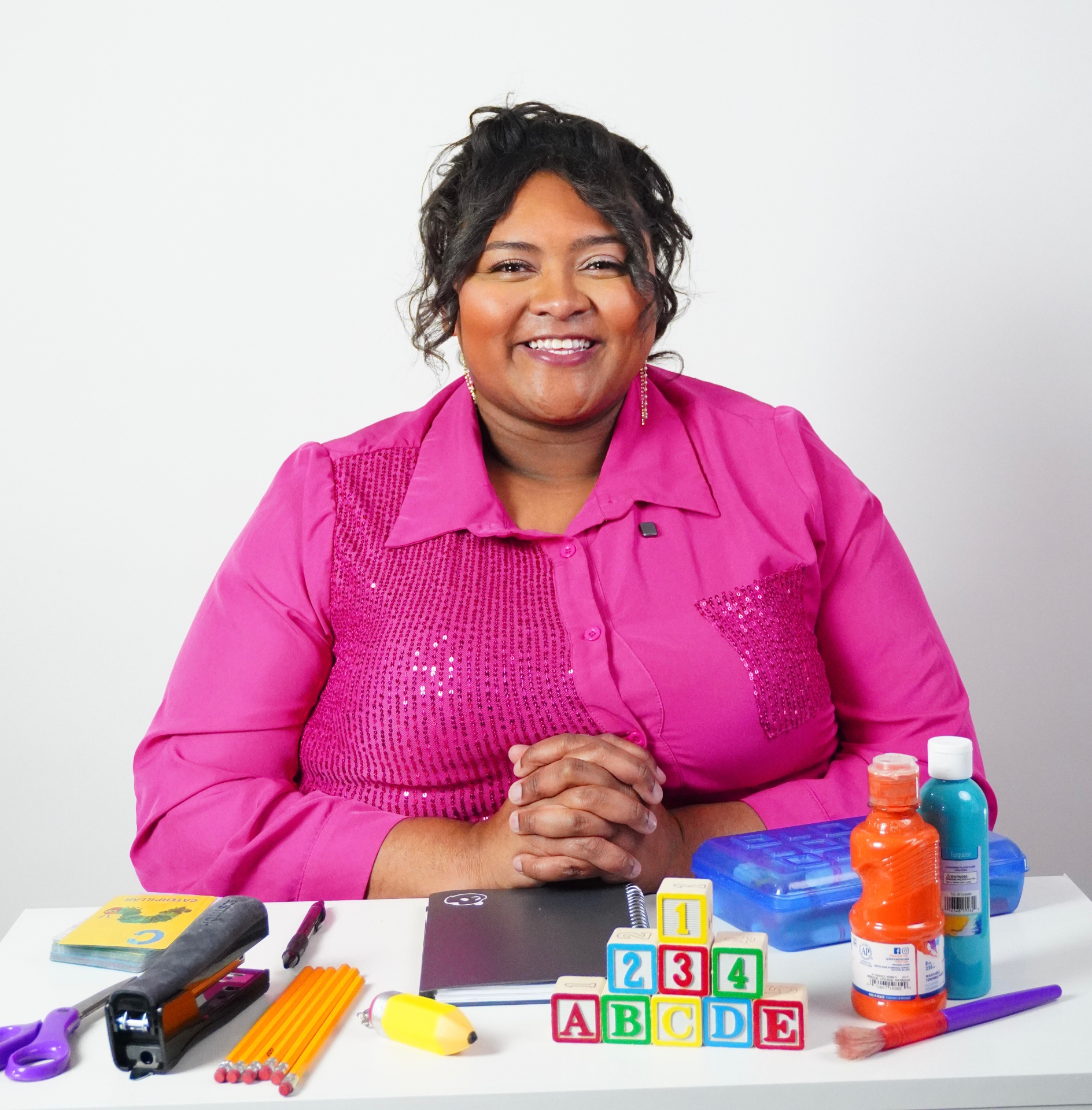 Ms. Hanna in a pink blazer surrounded by educational supplies